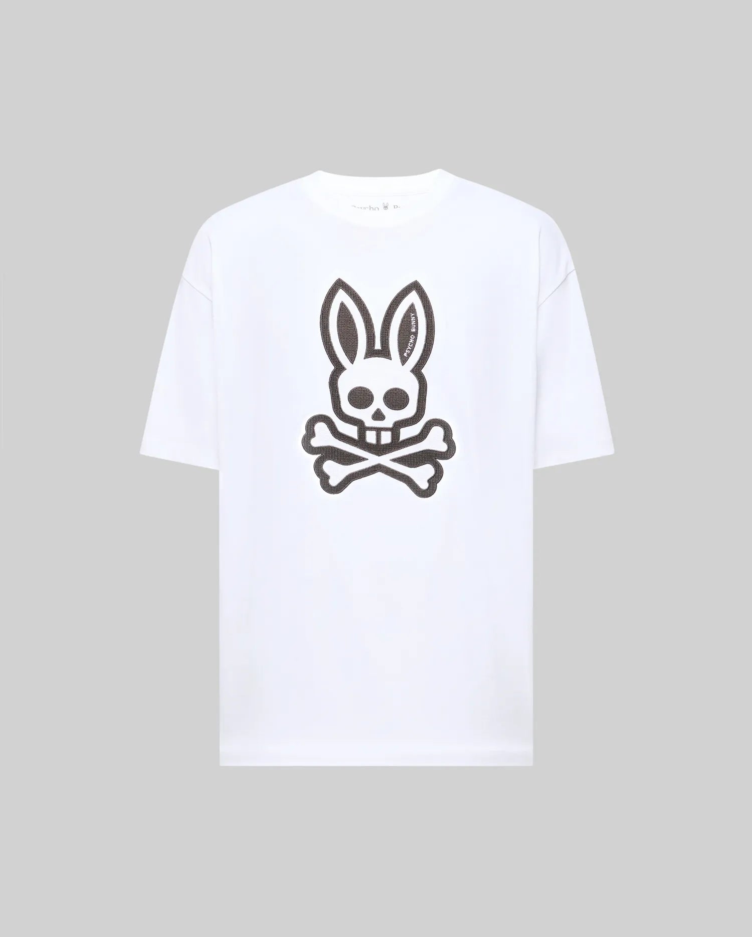 The Psycho Bunny MENS RYDER OVERSIZED TEE (MT0200062) features a bold black skull with bunny ears and crossed bones graphic on premium white Pima cotton, shown against a plain light gray background.