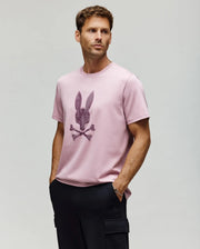 A man in a Psycho Bunny MENS GRANT BUNNY GRAPHIC TEE – MT0200081, crafted from soft Pima cotton.
