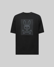The Psycho Bunny MENS REECE OVERSIZED TEE (MT0200082) is a black relaxed fit shirt with a dark gray bunny skull and crossbones graphic on the chest, presented on a light gray background.