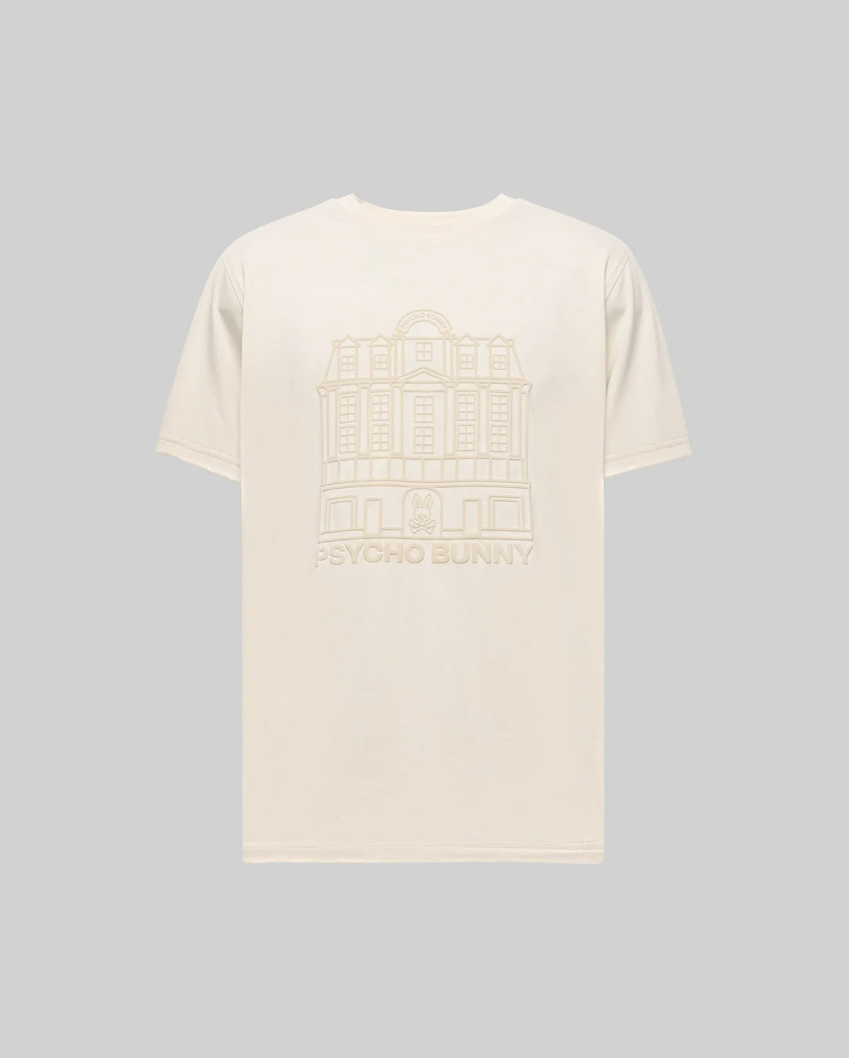 The Psycho Bunny MENS REDFORD GRAPHIC TEE (MT0200092) is a plain beige Pima cotton shirt with a subtle building line drawing and "PSYCHO BUNNY" text on the back, shown here against a light gray background.