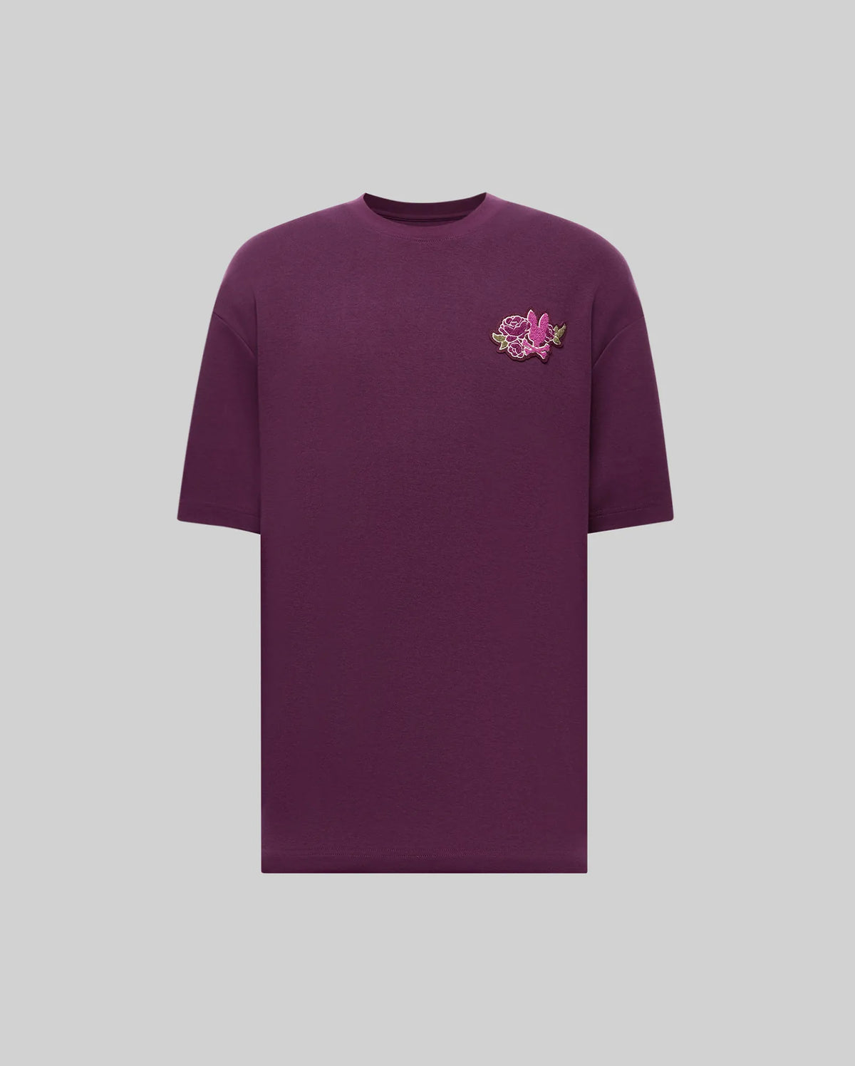 The Psycho Bunny MENS AUGUSTE OVERSIZED TEE (MT0200104) is a relaxed-fit, short-sleeve purple shirt with a pink and green embroidered rose on the left chest, shown on a light gray background—perfect for laidback style.