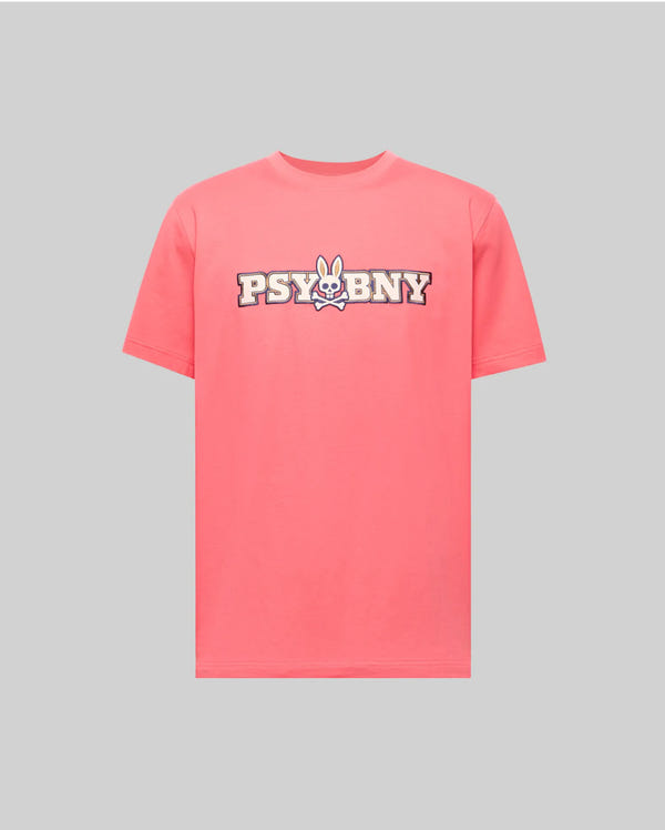 The Psycho Bunny MENS WADE GRAPHIC TEE (MT0200105) is a pink, 100% cotton short-sleeve tee with "PSYCHBNY" and a cartoon bunny face printed in bold on the chest. Regular fit, shown on a light gray background.