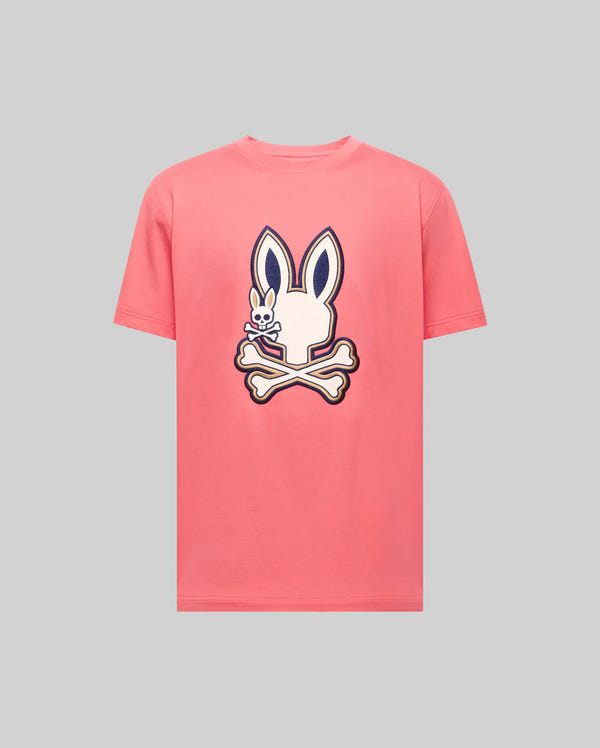 The Psycho Bunny MENS WADE GRAPHIC TEE (MT0200106) is a pink tee in 100% cotton, featuring a large white bunny head with dark ears above crossed bones, boldly outlined and centered on the light gray front.