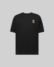 The Psycho Bunny MENS WADE OVERSIZED CHEST TEE (MT0200152) is a black, relaxed-fit short-sleeve Pima cotton shirt featuring a small white bunny and crossbones graphic on the upper left back, shown on a plain gray background.