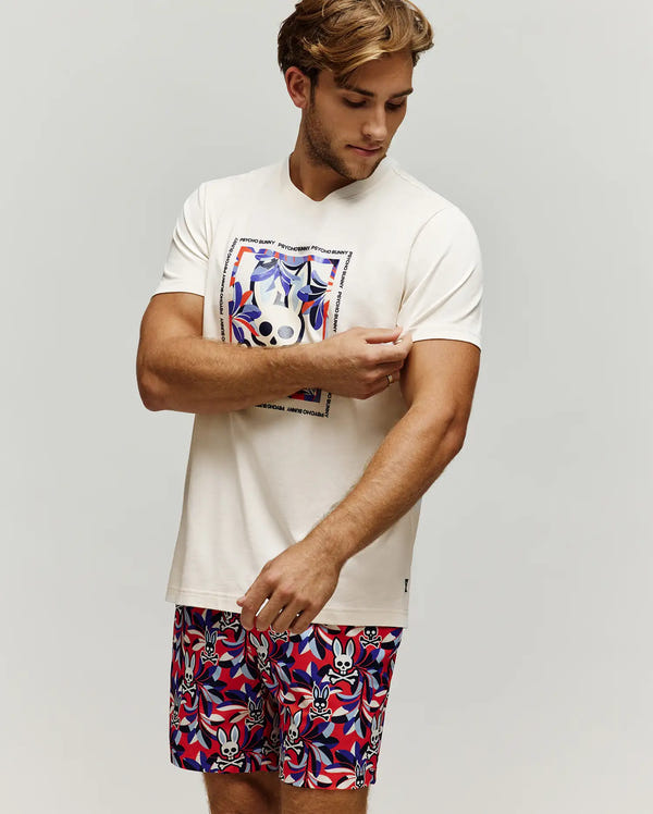Mens Florian Graphic Tee, cream jersey, classic fit, with a large chest graphic of a colorful bunny skull and floral design, framed by Psycho Bunny text. Red, blue, white shorts with all-over bunny skull and leaf print.