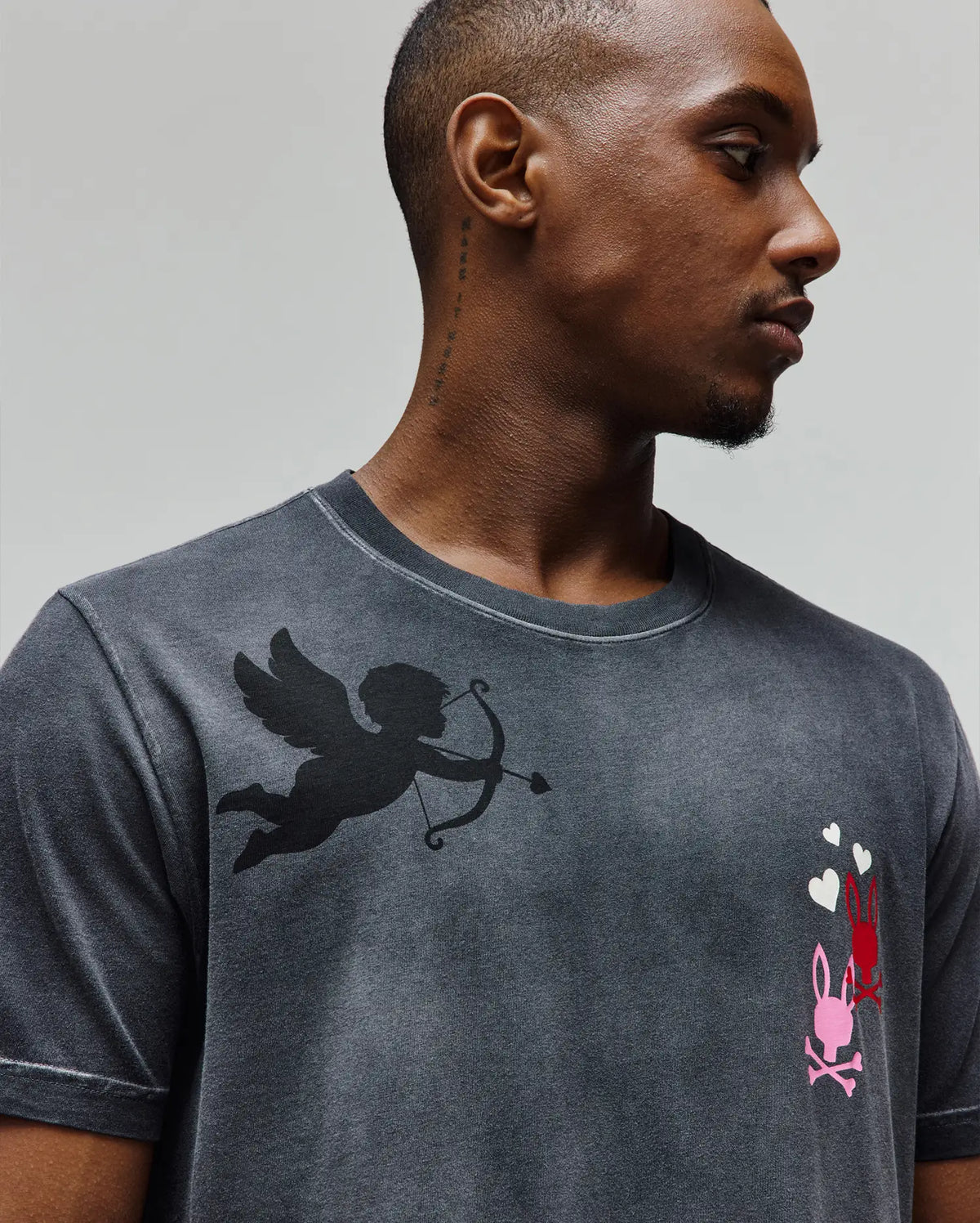 Mens Jack Graphic Tee in washed charcoal jersey, featuring a large black Cupid graphic on the left chest and smaller pink/red Psycho Bunny logos with white hearts on the right.