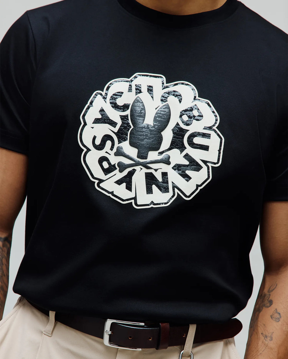 Mens Toby Graphic Tee. Black jersey knit t-shirt featuring a large central white and textured black Psycho Bunny skull and crossbones graphic, encircled by bold Psycho Bunny text. Refined streetwear, classic fit.