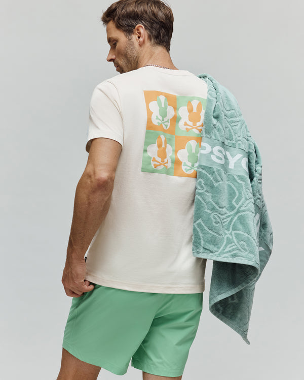 Mens Aiden Back Graphic Tee, cream jersey t-shirt with a classic fit, featuring a large back graphic of alternating orange and light green squares, each containing a white flower and a Psycho Bunny skull logo.