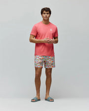 Mens Aiden Back Graphic Tee in coral jersey with a small white embroidered Psycho Bunny logo on the chest, paired with multi-color checkerboard print shorts featuring various bunny skull graphics.