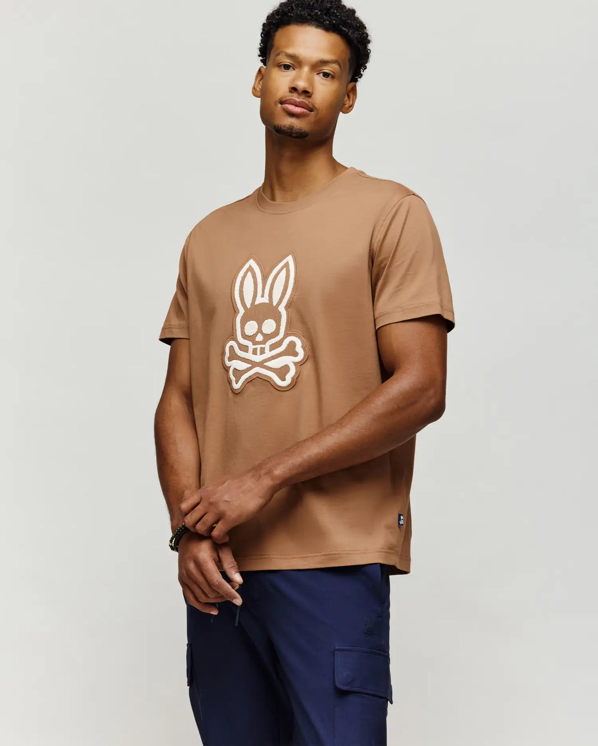 Mens Harley Graphic Tee, a classic fit camel brown jersey t-shirt featuring a large, textured white Psycho Bunny skull logo centered on the chest, with a small woven tag on the left hem.