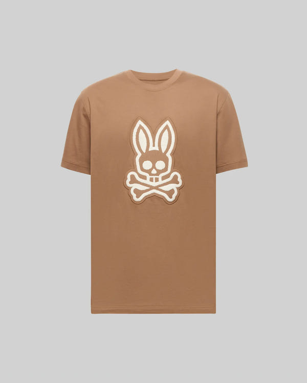 Mens Harley Graphic Tee, a classic fit tan jersey t-shirt with a prominent textured cream embroidered Psycho Bunny skull logo centered on the chest.