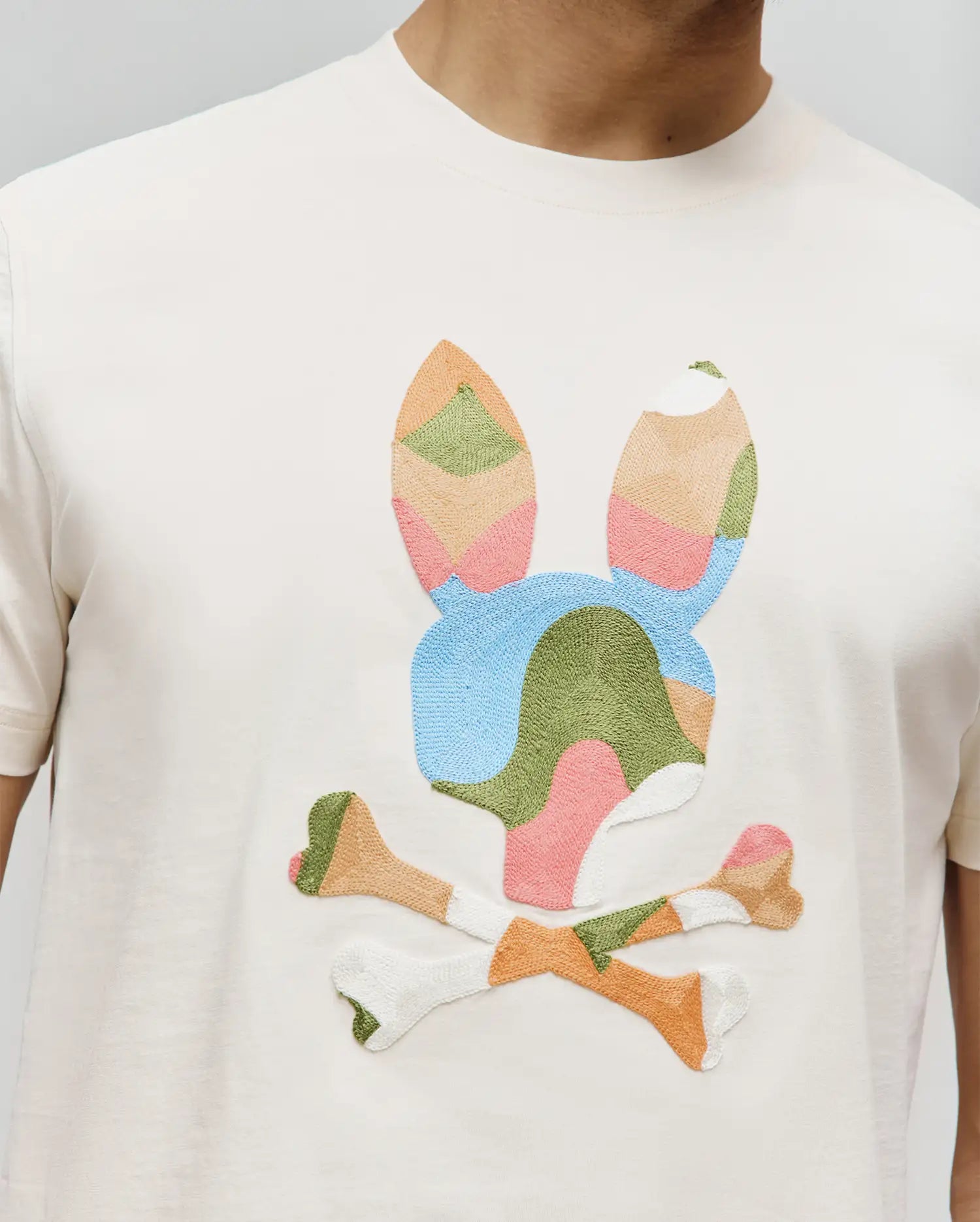Mens Ara Graphic Tee, cream classic fit jersey t-shirt with a large, embroidered multicolor patchwork bunny skull logo on the chest, featuring pastel blue, green, pink, orange, and white.