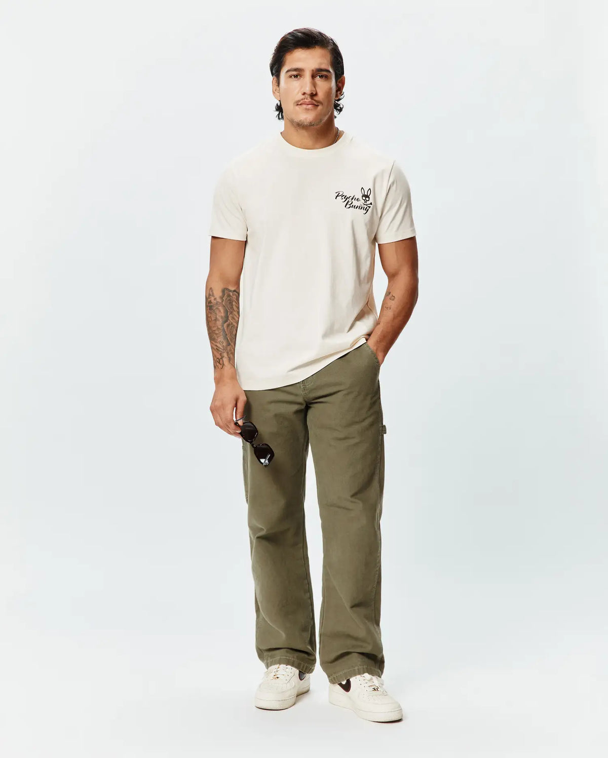 Mens Colin Back Graphic Tee, a classic fit ecru jersey t-shirt featuring a small, bold black Psycho Bunny skull logo and text printed on the left chest. (4)