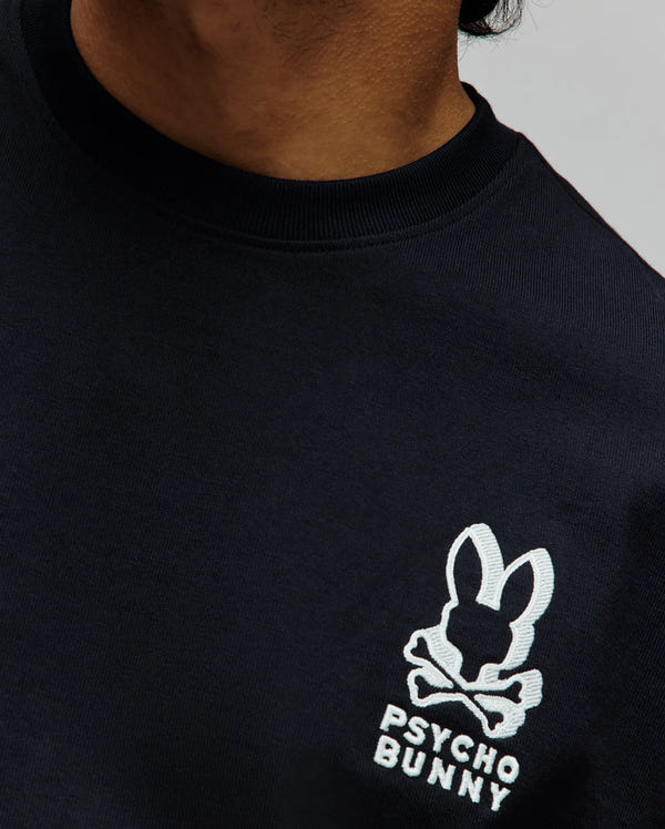 Mens Toby Oversized Tee in navy jersey knit, featuring an oversized fit, ribbed crew neck, and a prominent embroidered white Psycho Bunny skull and crossbones logo with text on the left chest.
