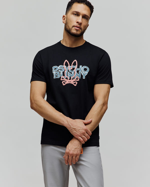 Mens Herman Graphic Tee, black classic fit jersey t-shirt with a large textured pink and light blue Psycho Bunny text and skull logo graphic on the chest.