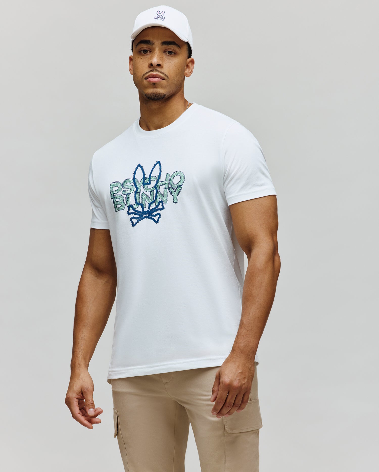 White Mens Herman Graphic Tee, a classic fit jersey t-shirt with a large, distressed blue and green Psycho Bunny text and iconic bunny skull logo graphic on the chest.