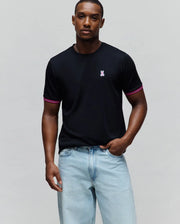 Mens Clark Performance Tee in black, featuring a classic fit, smooth jersey knit, pink and white striped ribbed cuffs, and an embroidered pink and white Psycho Bunny skull logo on the left chest.