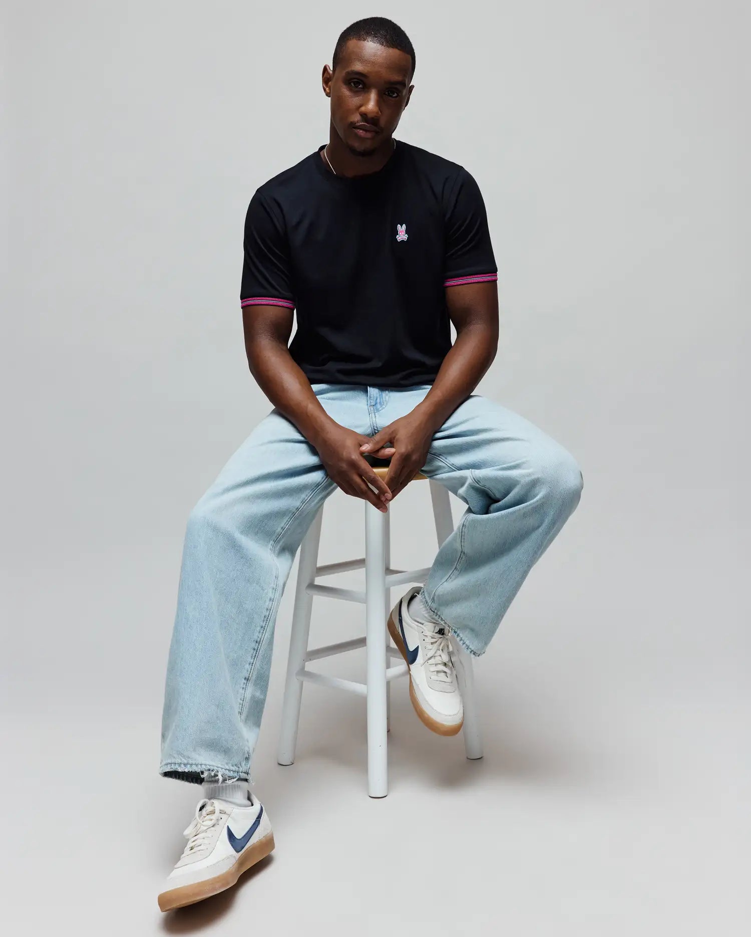 Mens Clark Performance Tee, a black classic fit jersey knit t-shirt with a small embroidered pink Psycho Bunny skull logo on the left chest and pink striped ribbed cuffs.