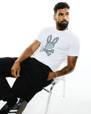 Mens Jaden Applique Graphic Tee, a classic fit white jersey t-shirt featuring a large grey and black Psycho Bunny skull and crossbones logo with a mini bunny skull pattern on the chest. (4)