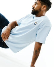 Mens Jaydon Pima Cotton Oversized-Fit Tee in light blue, featuring a smooth jersey texture and a vibrant orange, white, and blue embroidered Psycho Bunny skull logo on the left chest. (3)