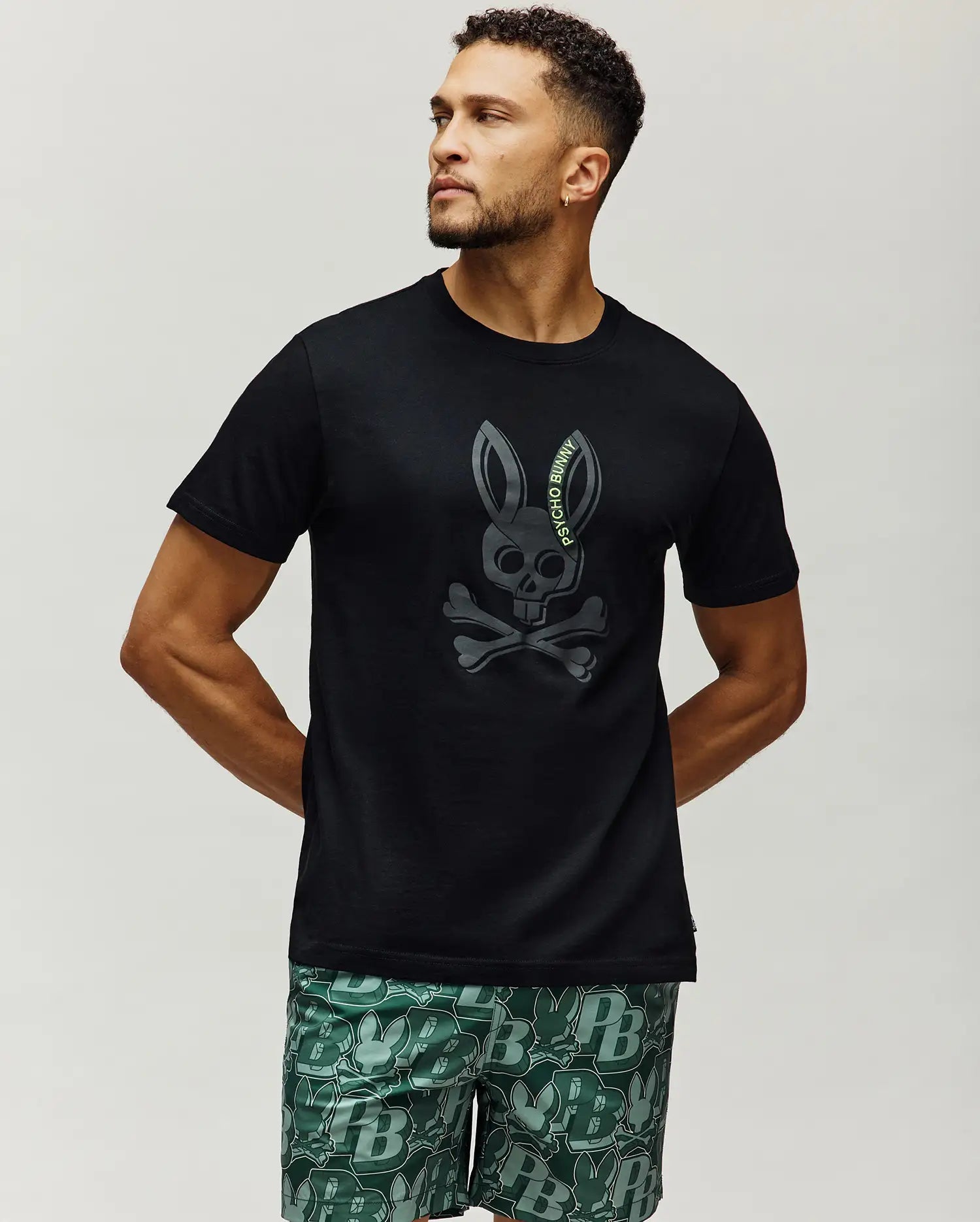 Mens Serge Embroidered Bunny Graphic Tee, a classic fit black jersey t-shirt featuring a large dark grey embroidered Psycho Bunny skull and crossbones graphic with neon green text on the chest.