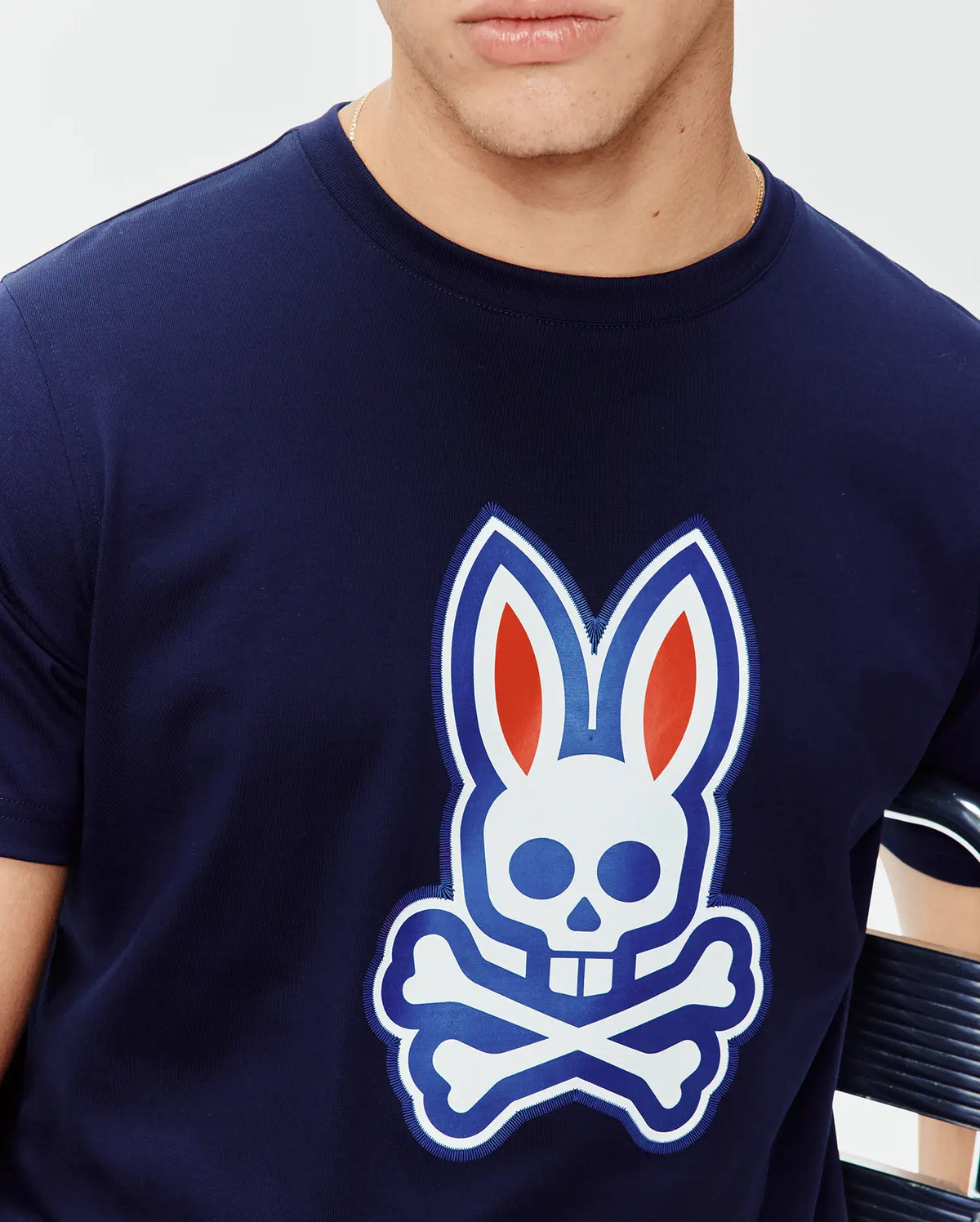 Mens John Graphic Tee, a navy blue classic fit jersey knit t-shirt featuring a large central chest graphic of the iconic Psycho Bunny skull logo in white, blue, and red with an embroidered outline. (4)