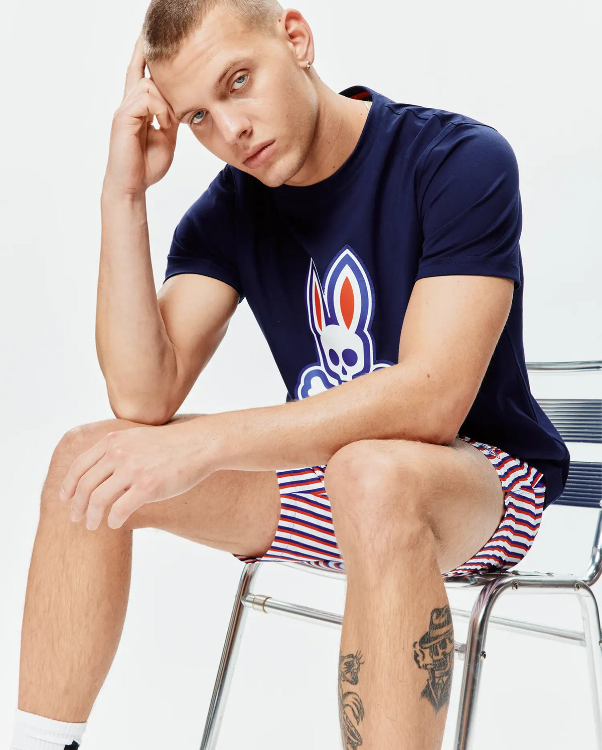 Mens John Graphic Tee, navy jersey, large white, red, blue Psycho Bunny skull logo on chest, paired with relaxed fit white, red, blue striped shorts. (3)