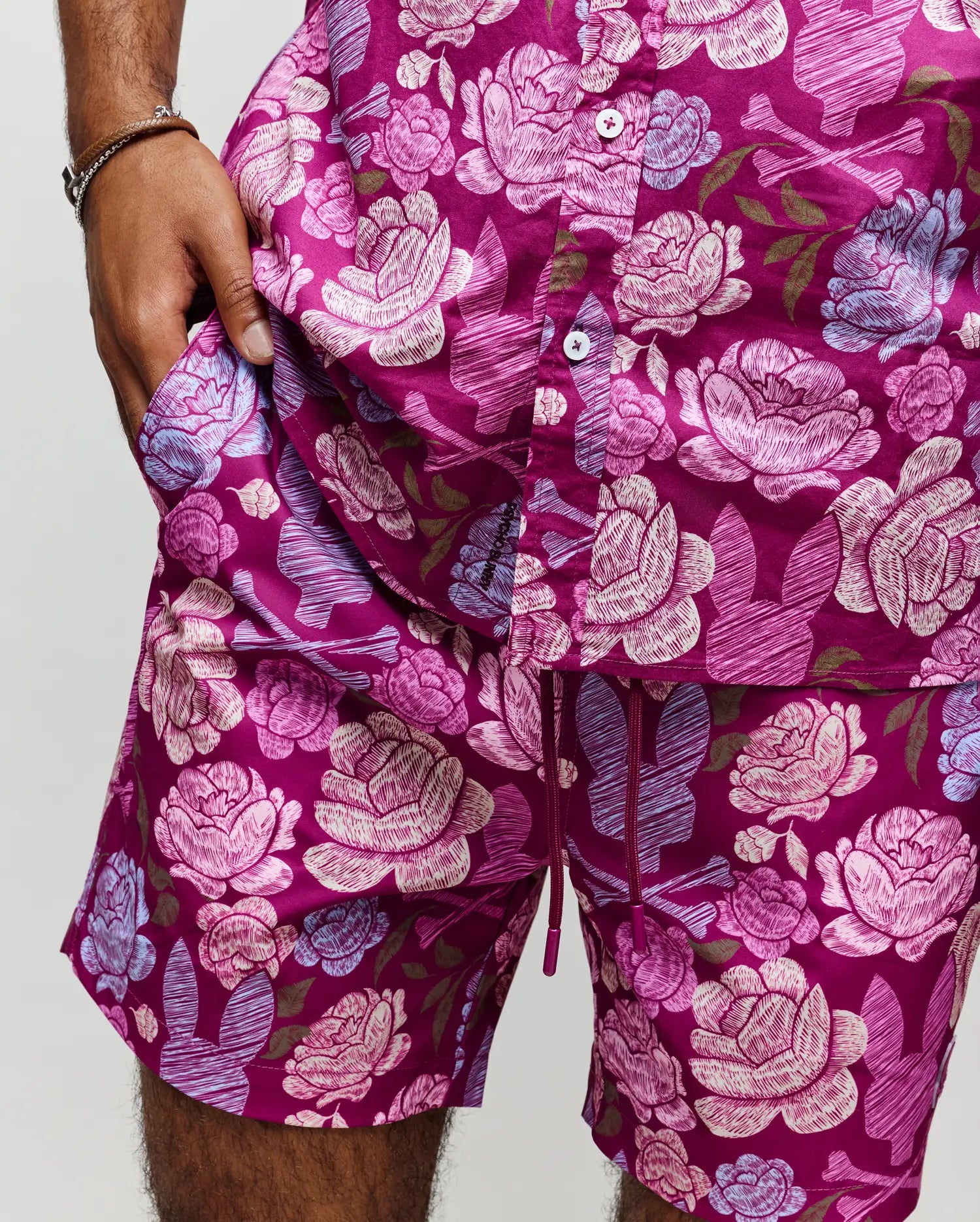 Wearing Psycho Bunny’s MENS ROWEN SHIRT - MT0300038, a person in matching magenta shorts is shown with one hand in their pocket, displaying only their lower torso and upper legs.