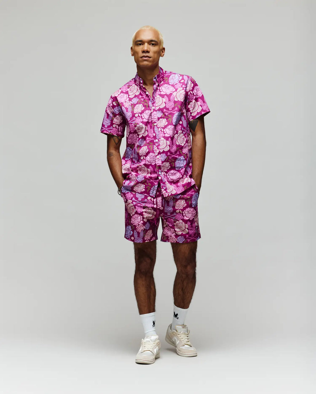 A person stands facing forward in the Psycho Bunny MENS ROWEN SHIRT - MT0300038, paired with white socks and sneakers, against a plain light gray background.