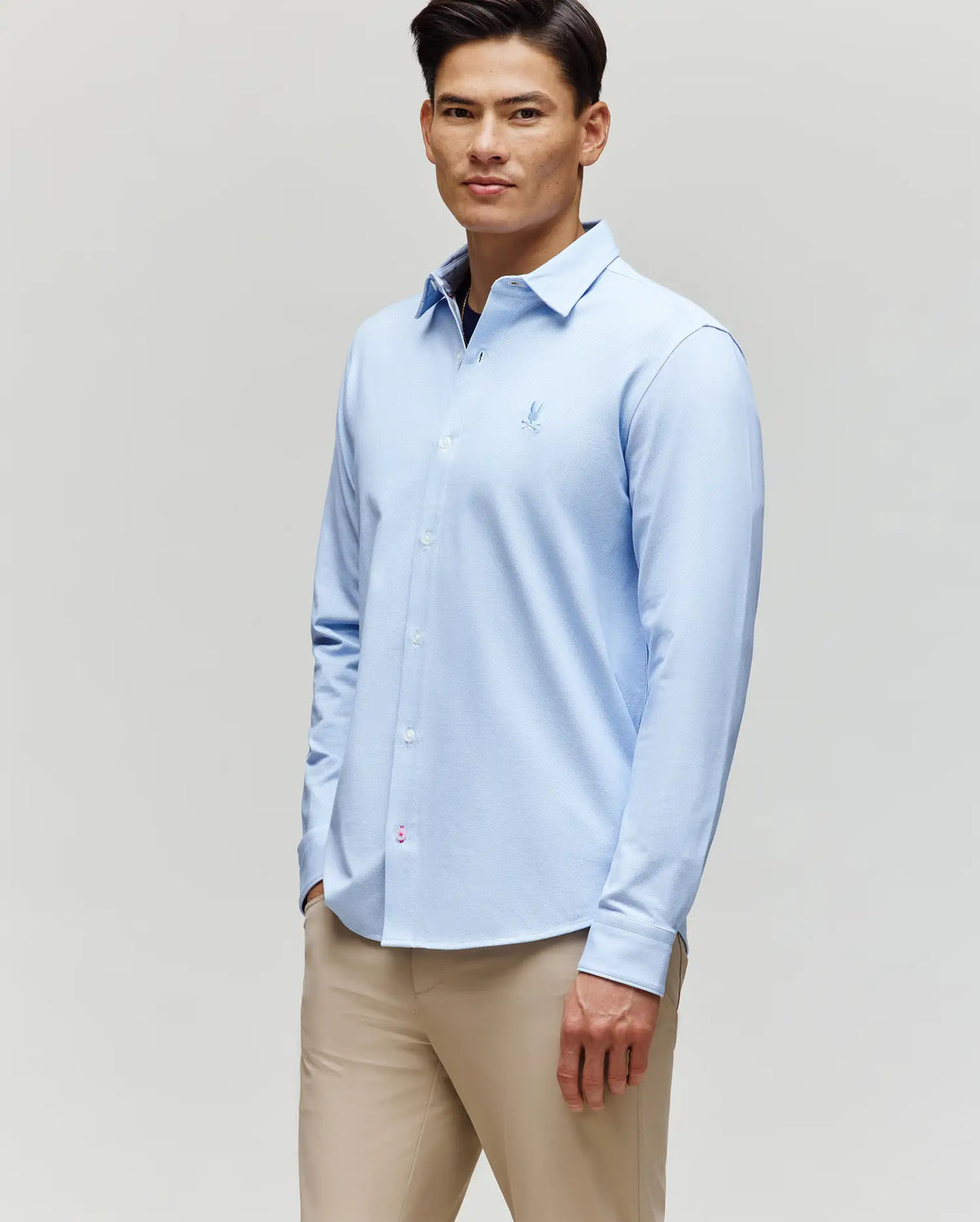 A man wearing the Psycho Bunny MENS JIM JERSEY STRIPED KNIT SHIRT (MT0300041) and beige pants stands against a plain light background, looking forward with a relaxed expression.