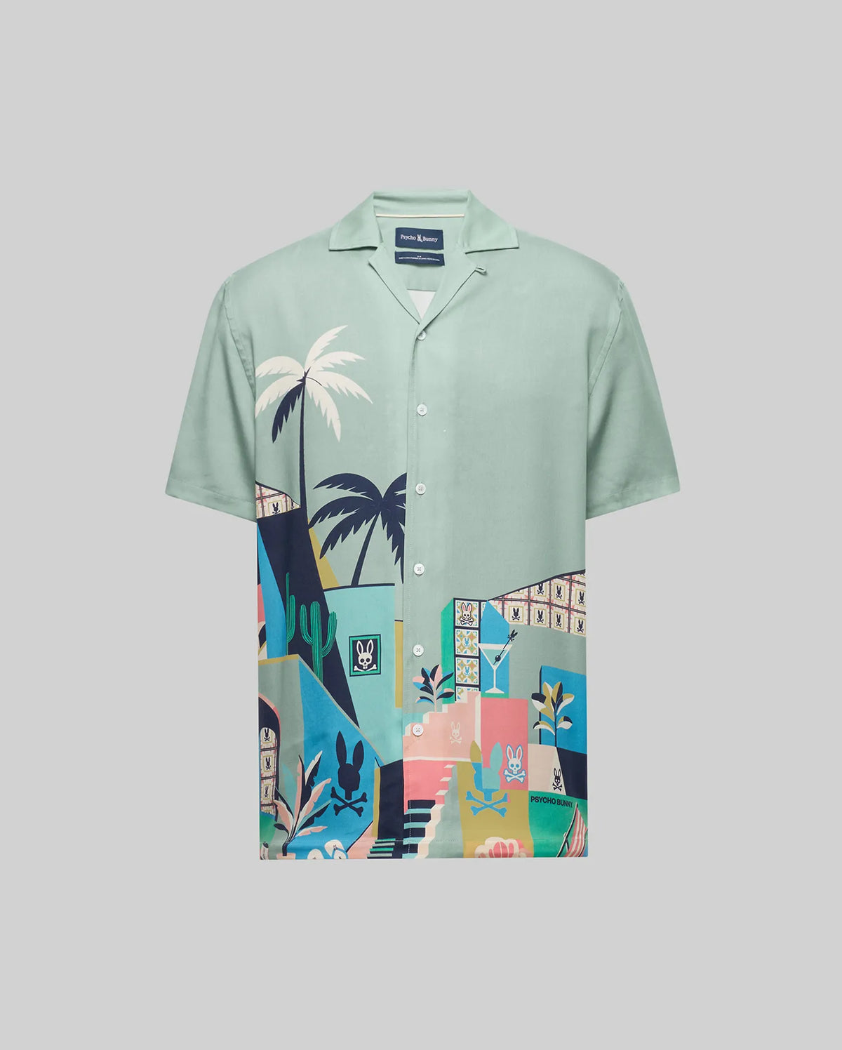The Psycho Bunny MENS BLAISE TENCEL SHIRT (MT0300056) is a light green, short-sleeve button-up with a breathable Tencel fabric and a vibrant tropical design featuring plants, stairs, and playful animal illustrations on the lower half.