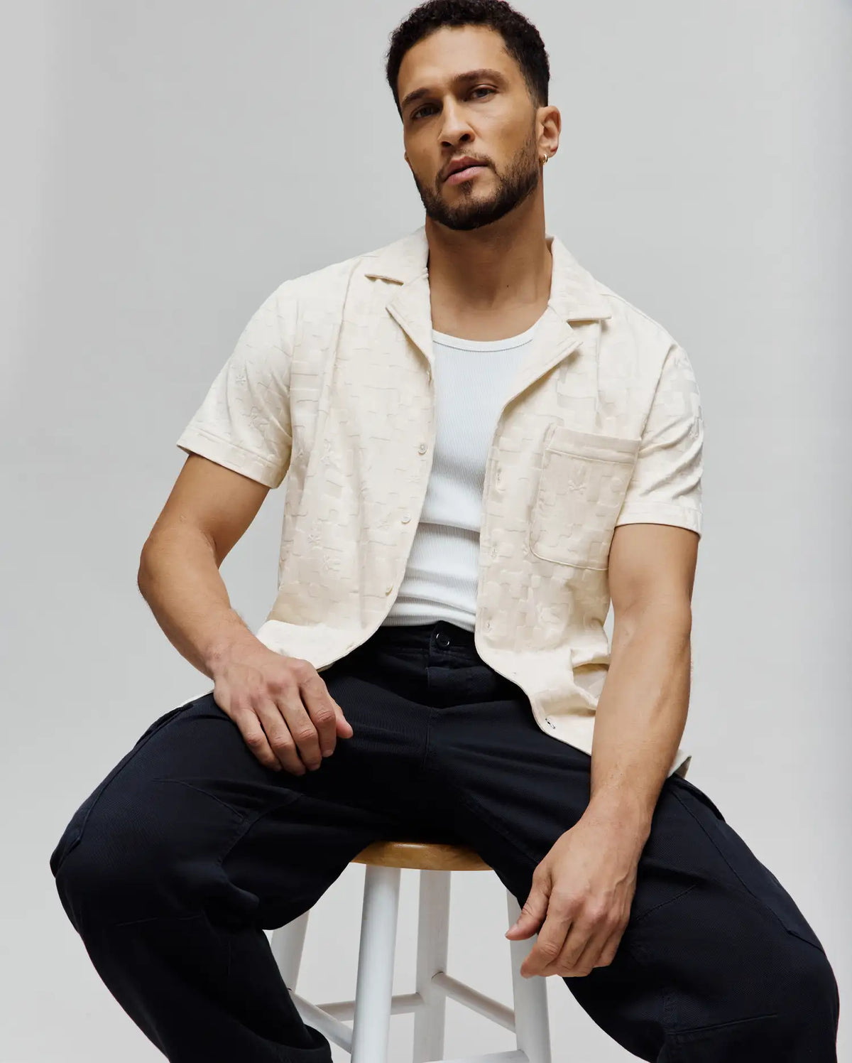 Mens Josh Jacquard Shirt, a cream short-sleeve button-up with a relaxed fit, open collar, and subtle all-over Psycho Bunny skull jacquard pattern, featuring a single chest pocket.