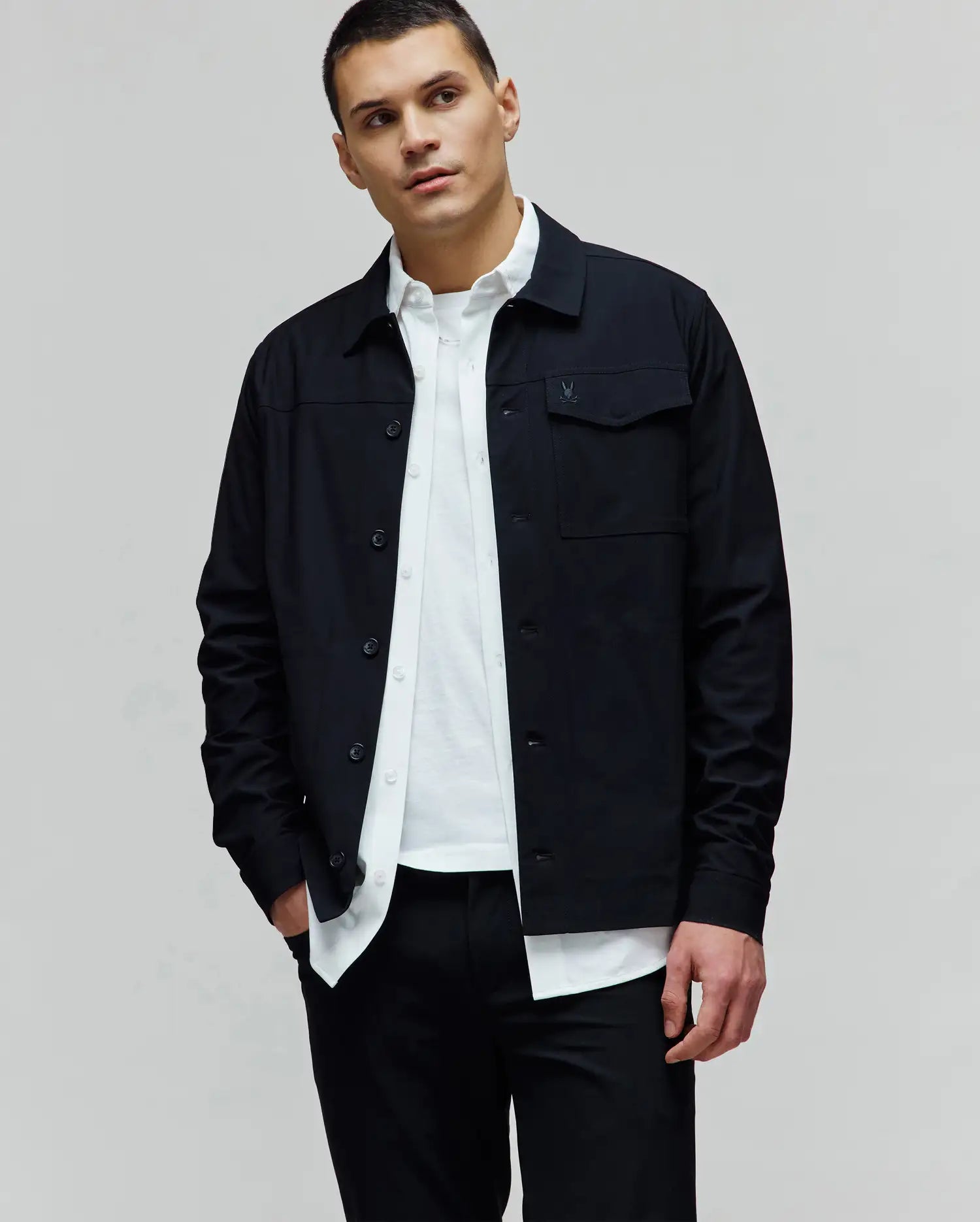 Black Mens Maverick Overshirt, classic fit, smooth fabric, with a button-front, pointed collar, two chest flap pockets, and a small embroidered black Psycho Bunny skull logo on the left pocket.