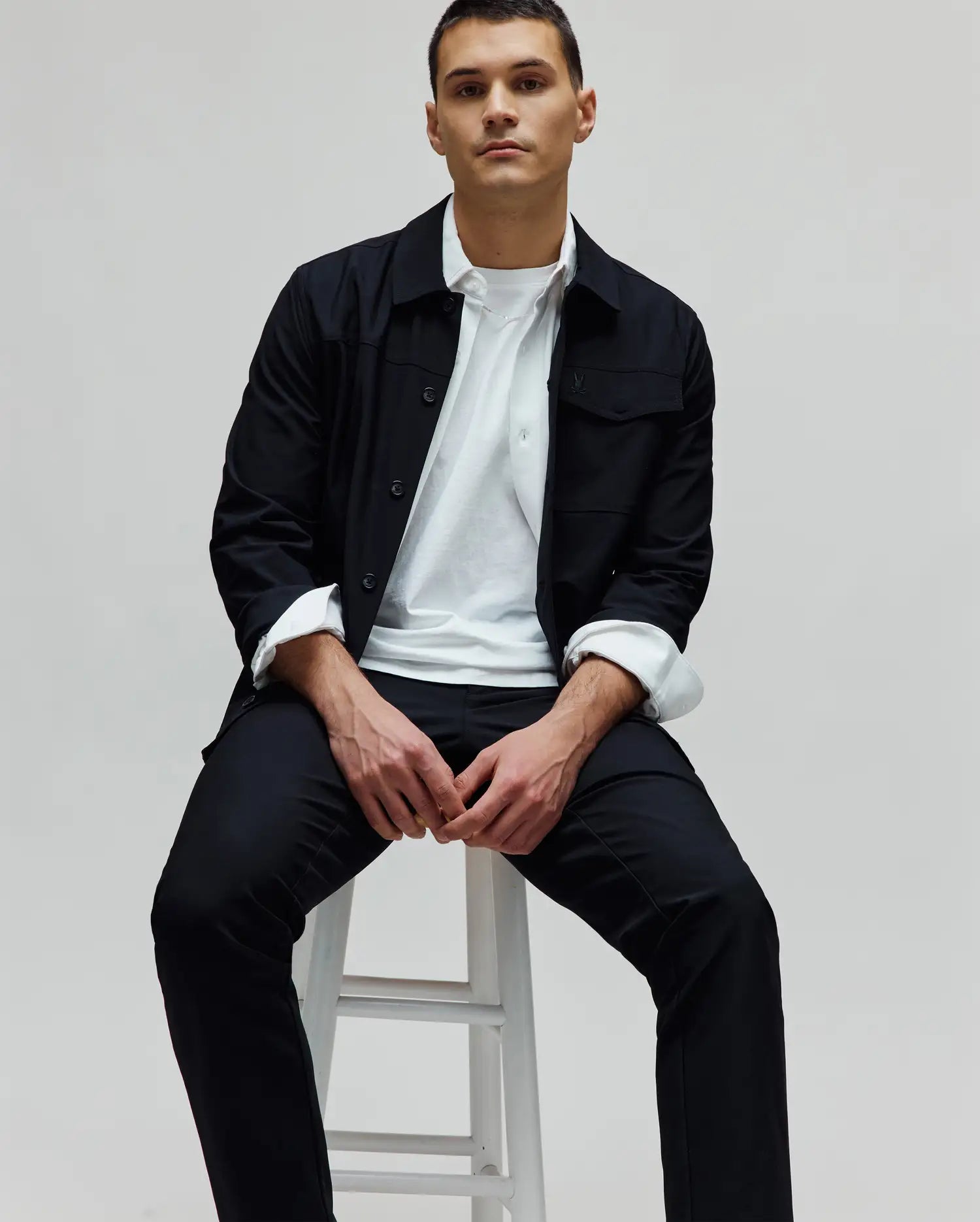 Mens Maverick Overshirt in black, featuring a classic fit, smooth fabric, button-front, and chest pockets with a small embroidered Psycho Bunny skull logo on the left. Layered over a white t-shirt.