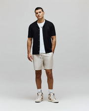 Mens Xandros Knit Shirt, a black classic fit short-sleeve knit shirt featuring a subtle geometric texture, full button-front, and a small embroidered Psycho Bunny skull logo on the left chest.