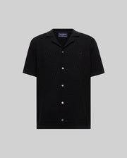 Mens Xandros Knit Shirt, black short-sleeve with a subtle geometric knit pattern, spread collar, white buttons, and a small embroidered black Psycho Bunny skull logo on the chest.
