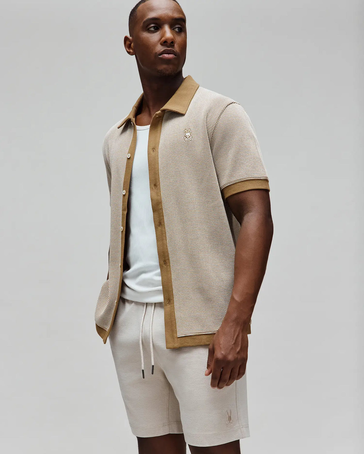 Mens Maxton Waffle Shirt, a relaxed fit, short-sleeve, collared button-front in beige waffle knit with brown trim and a small embroidered Psycho Bunny skull logo on the left chest.