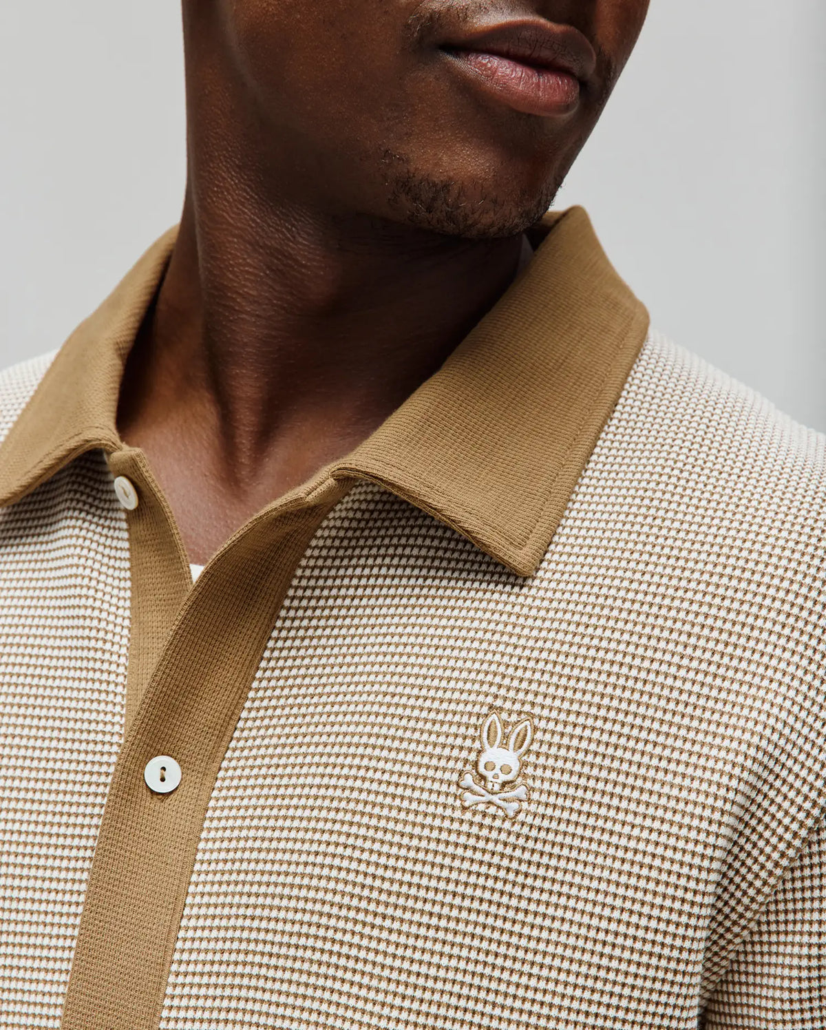 Mens Maxton Waffle Shirt in a cream and tan textured waffle knit, featuring a solid tan collar and placket with white buttons, and a small embroidered cream Psycho Bunny skull logo on the left chest.