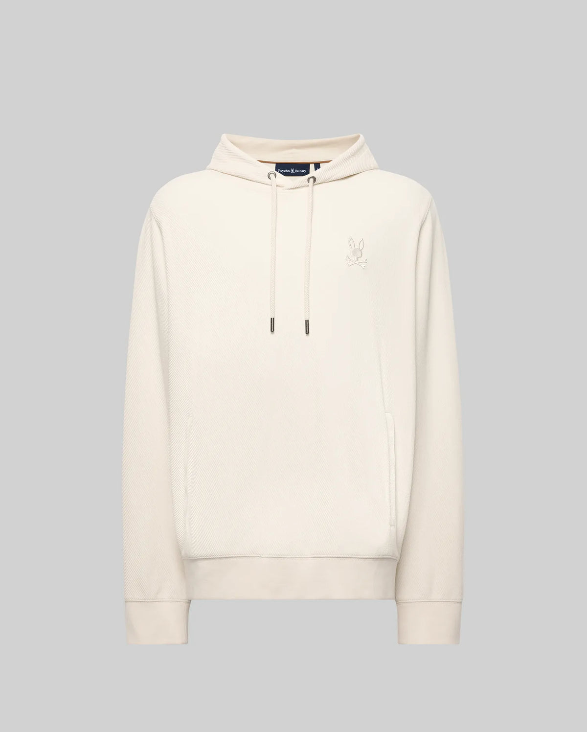 The Psycho Bunny MENS KAI HOODIE - MT0500019 is a plain light beige hoodie with long sleeves, a front pocket, and a small embroidered Bunny logo on the left chest, shown against a solid light grey background.