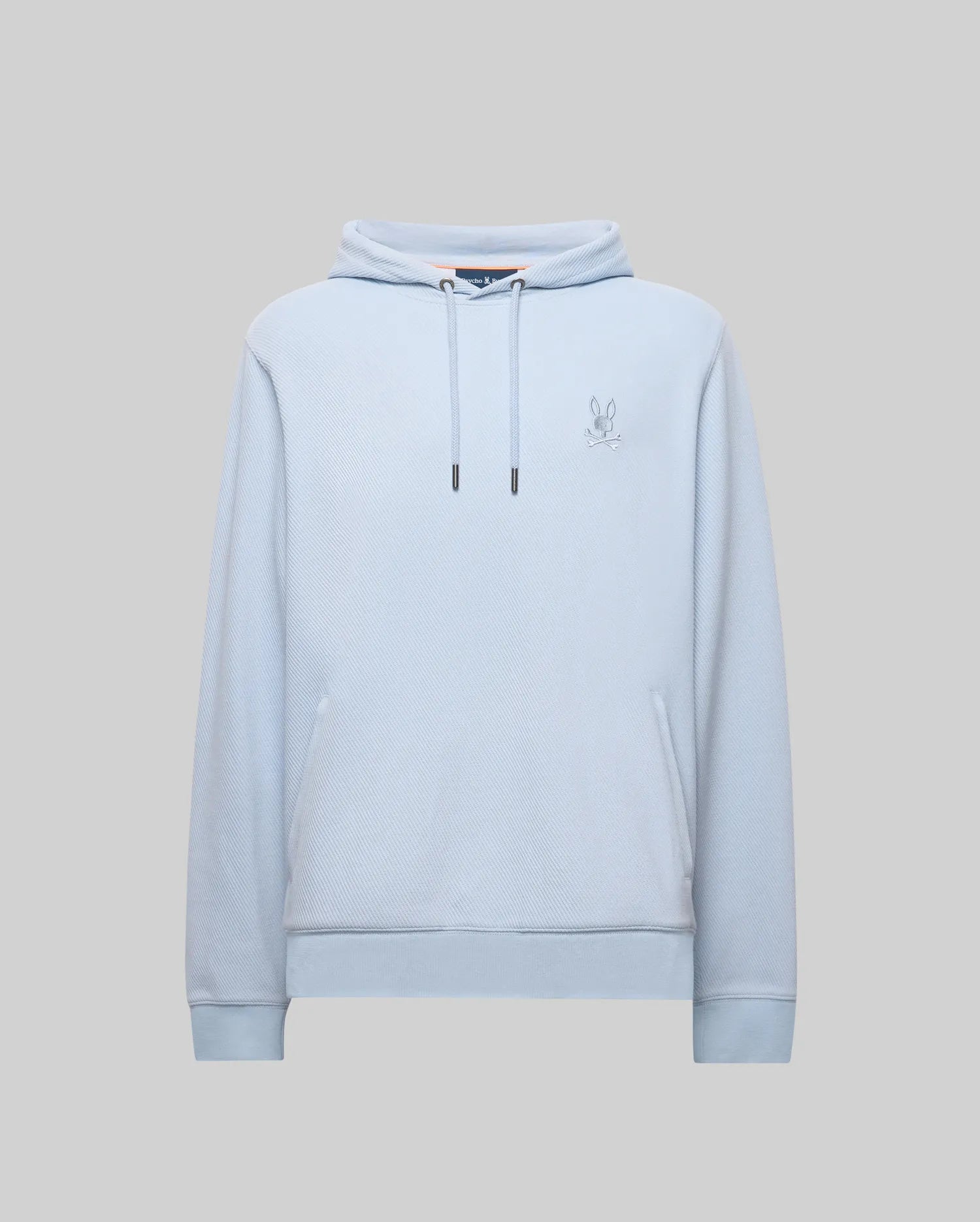 The Psycho Bunny MENS KAI HOODIE - MT0500019 features a light blue twill texture, front pocket, drawstrings, and an embroidered Bunny logo on the left chest, shown against a gray background.