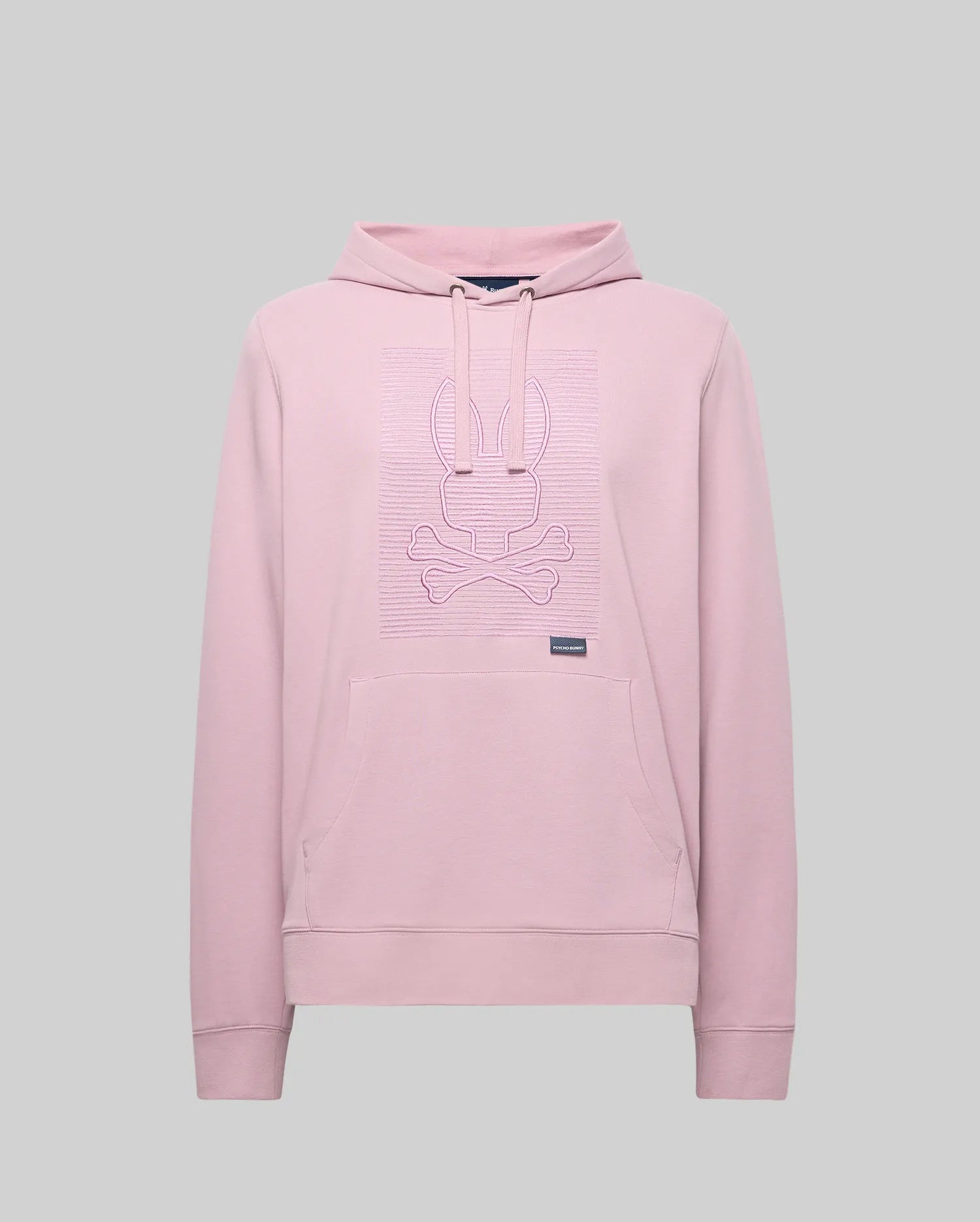 The Psycho Bunny MENS GRANT HOODIE - MT0500032 in light pink is crafted from a premium cotton blend, featuring a kangaroo pocket and a raised bunny head with crossed bones outline graphic on the chest. Background: plain light gray.