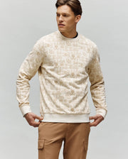 A man in a cream Psycho Bunny MENS REED FLOCK CREW (MT0500041) and tan cargo pants stands slightly turned to the side, hands on hips, against a light gray background.