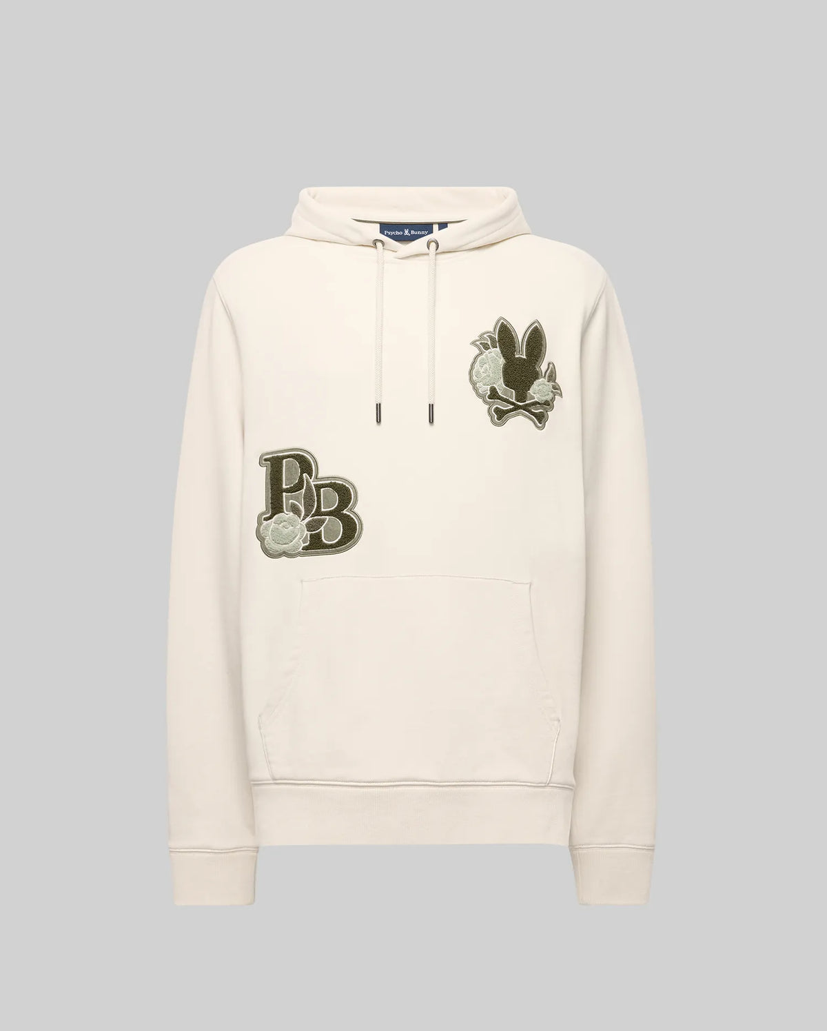 The Psycho Bunny MENS AUGUSTE HOODIE - MT0500043 is a cream-colored premium cotton hoodie with a front pocket, chenille floral detailing, an embroidered “PB” and flower patch on the left chest, plus a black bunny and flower patch on the right.