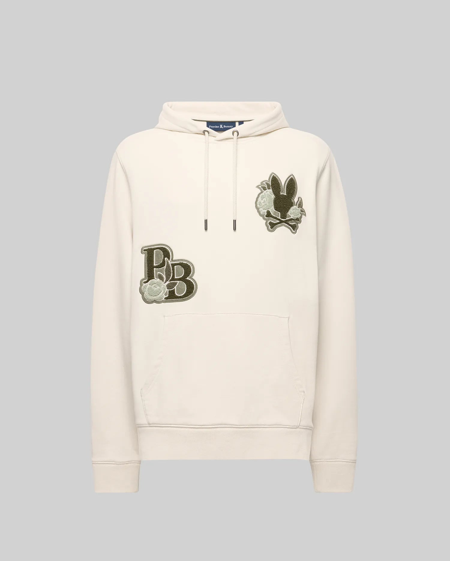 The Psycho Bunny MENS AUGUSTE HOODIE - MT0500043 is a cream-colored premium cotton hoodie with a front pocket, chenille floral detailing, an embroidered “PB” and flower patch on the left chest, plus a black bunny and flower patch on the right.