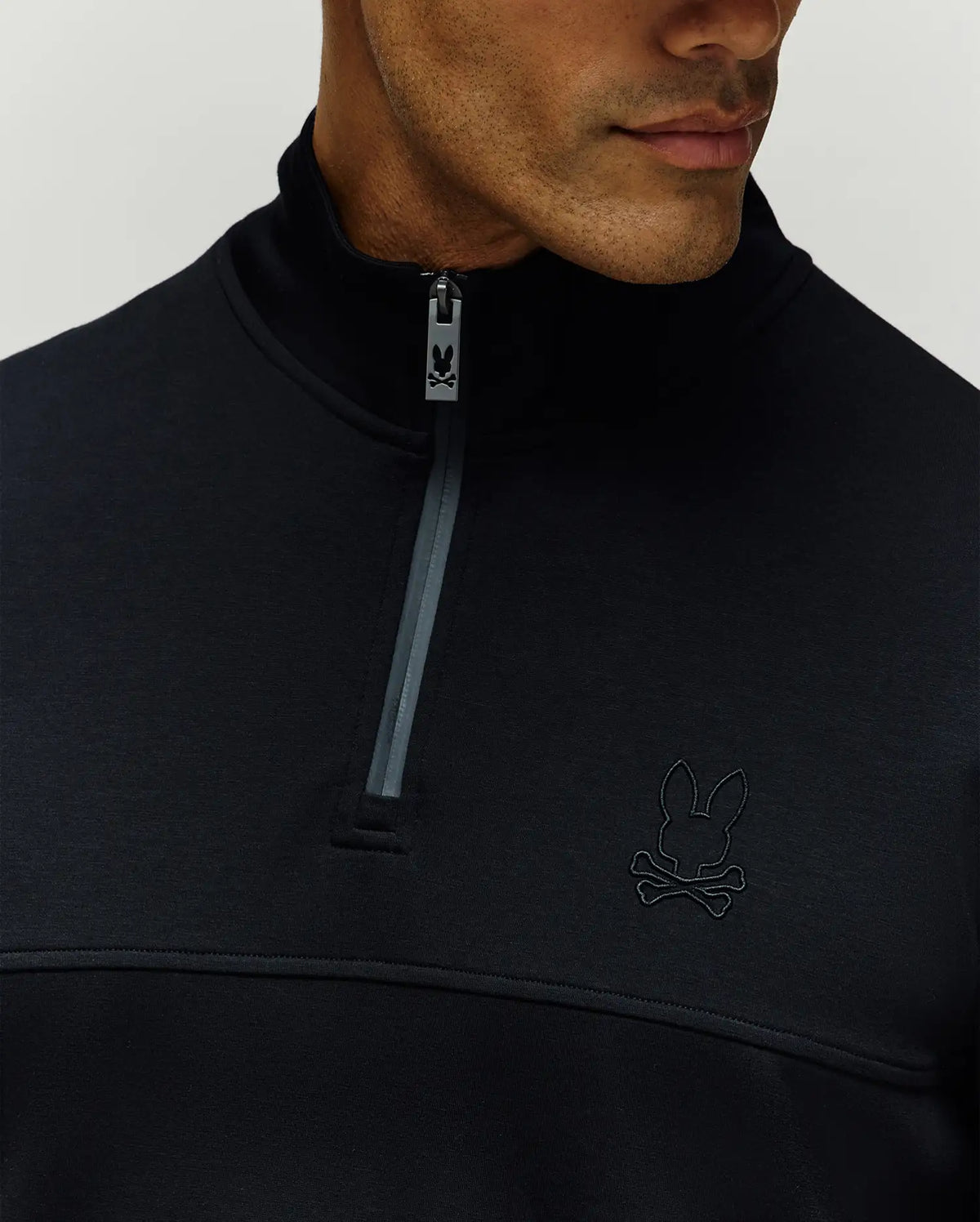 Mens Zeke 1/4 Mock Zip Pullover in black, classic fit, smooth fabric, dark grey 1/4 zip with Psycho Bunny logo pull, horizontal chest seam, and tonal embroidered bunny skull on left chest.