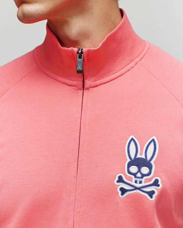 The Psycho Bunny MENS DAWSON TRACK JACKET (MT0500113) features a pink high-collar design with a large blue rabbit skull and crossbones patch on the chest—an athletic style upgrade for your wardrobe.