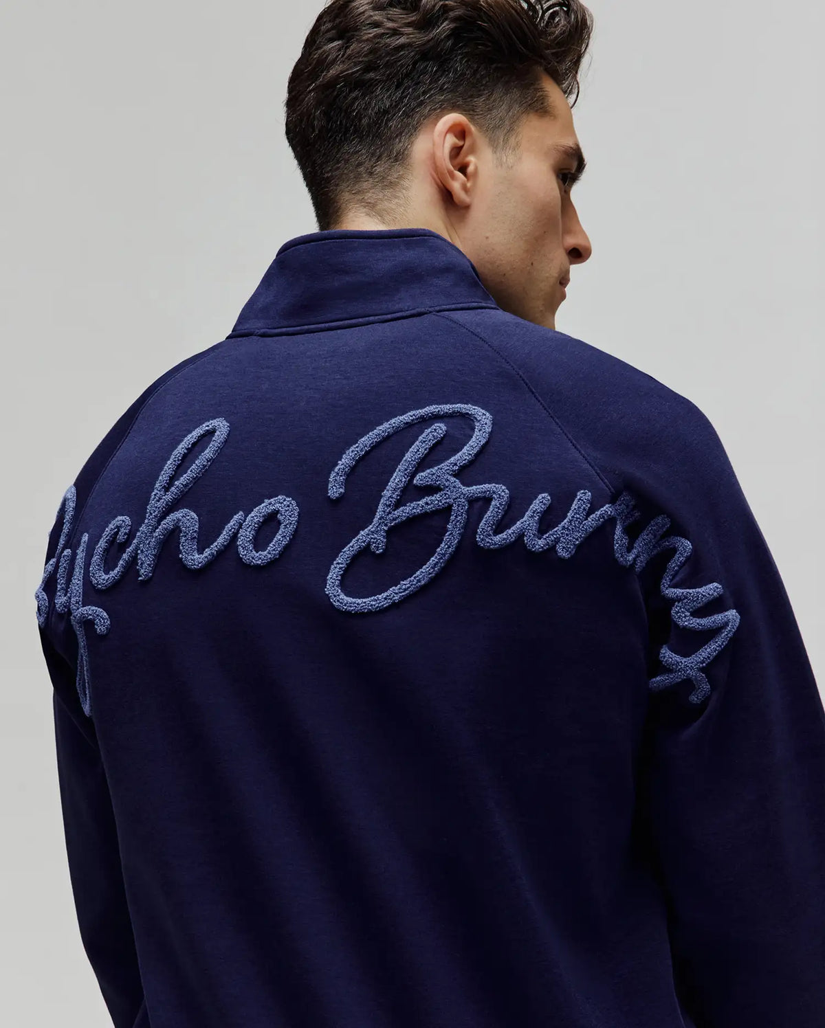 Mens Tate 1/4 Zip Chenille Pullover in navy, featuring a large, light blue chenille embroidered Psycho Bunny script across the upper back, with a smooth knit texture and relaxed fit.