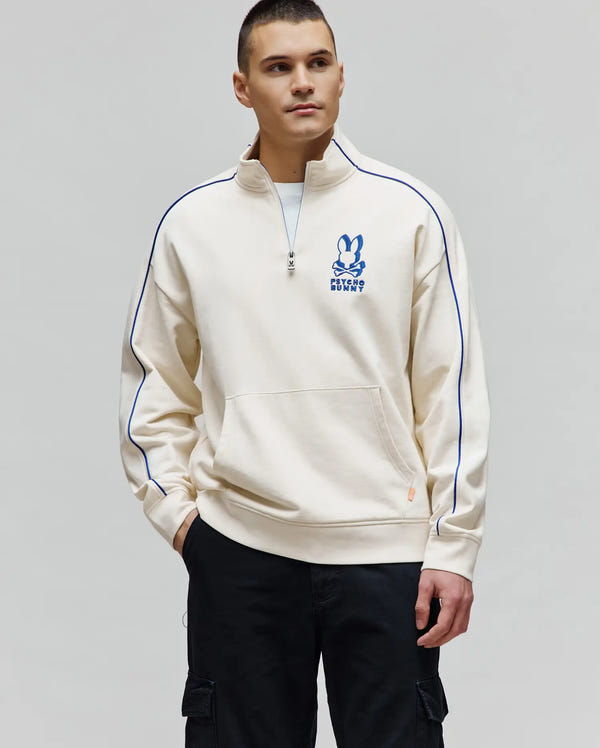Mens Toby 1/4 Zip cream French terry sweatshirt, featuring a relaxed fit, royal blue piping on sleeves and collar, a quarter zip, kangaroo pocket, and a large embroidered blue Psycho Bunny skull logo on the chest.