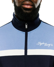 Jacques Pique Track Jacket in navy and light blue color-block pique, featuring a white horizontal stripe, embroidered white Psycho Bunny script logo on the left chest, and a bunny skull zipper pull. (4)