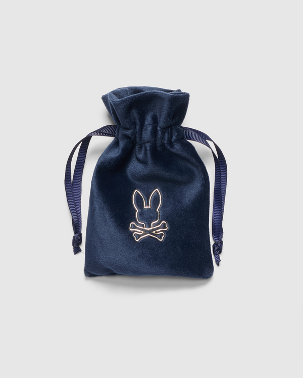 The PB ACCESSORY VELVET BAG - PBVLTBAG by Psycho Bunny is a navy blue velvet drawstring pouch featuring an embroidered rabbit and crossbones logo on the front. It includes dark blue ribbon ties and is showcased against a light gray background.